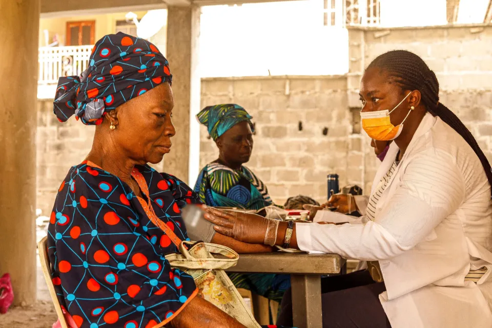 A health worker takes an older woman’s blood pressure at a community clinic table